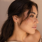 A woman with long dark hair and freckles wears shimmering Opal Inlay Earrings, gazing to the side against a beige background.