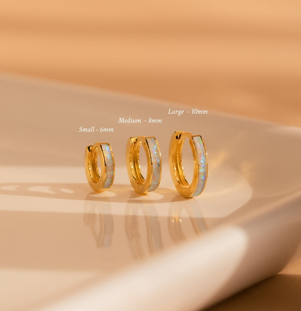 Three Opal Inlay Earrings in small, medium, and large sizes from our collection are displayed on a cream-colored surface.