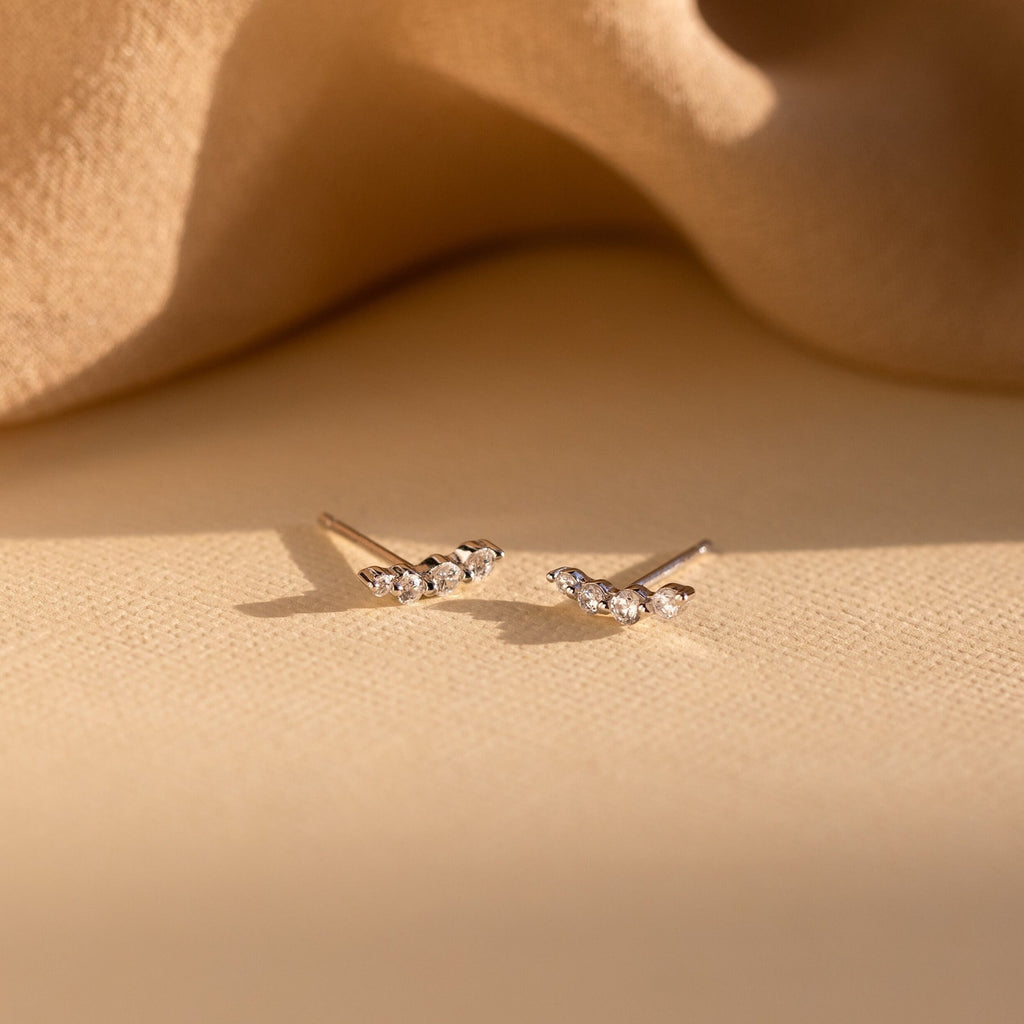 Tiny Diamond Climbers—delicate gold stud earrings featuring small sparkling stones on a soft beige fabric background—make an elegant gift for anniversaries.