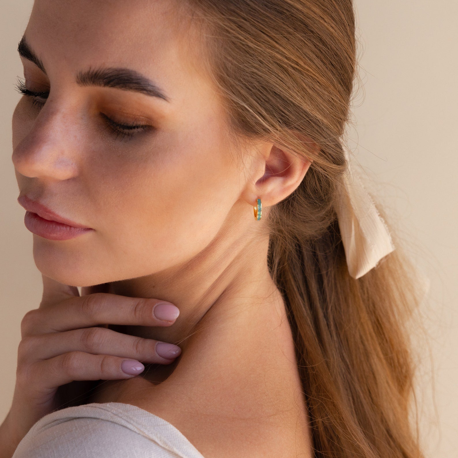 A woman with light brown hair in a ponytail wears the Opal Inlay Hoops Set, posing with her hand on her neck—an elegant bridal jewelry or wedding earring choice.