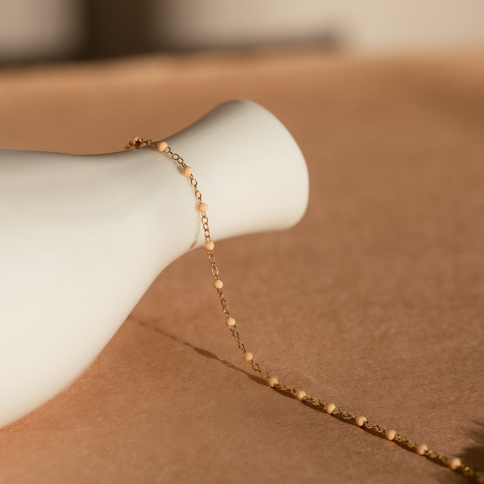 Peach Station Necklace elegantly displayed on a smooth white vase atop a soft beige surface.