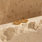 The Citrine Pave Huggies are displayed on a textured beige stone surface, their elegant hoops glowing in natural sunlight.
