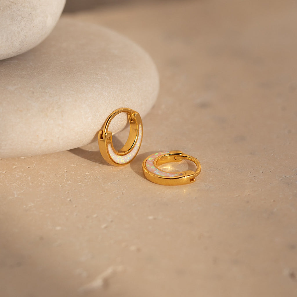 The Crescent Moon Opal Huggies glow elegantly atop a rock.