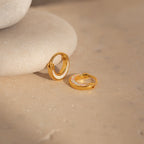 The Crescent Moon Opal Huggies glow elegantly atop a rock.