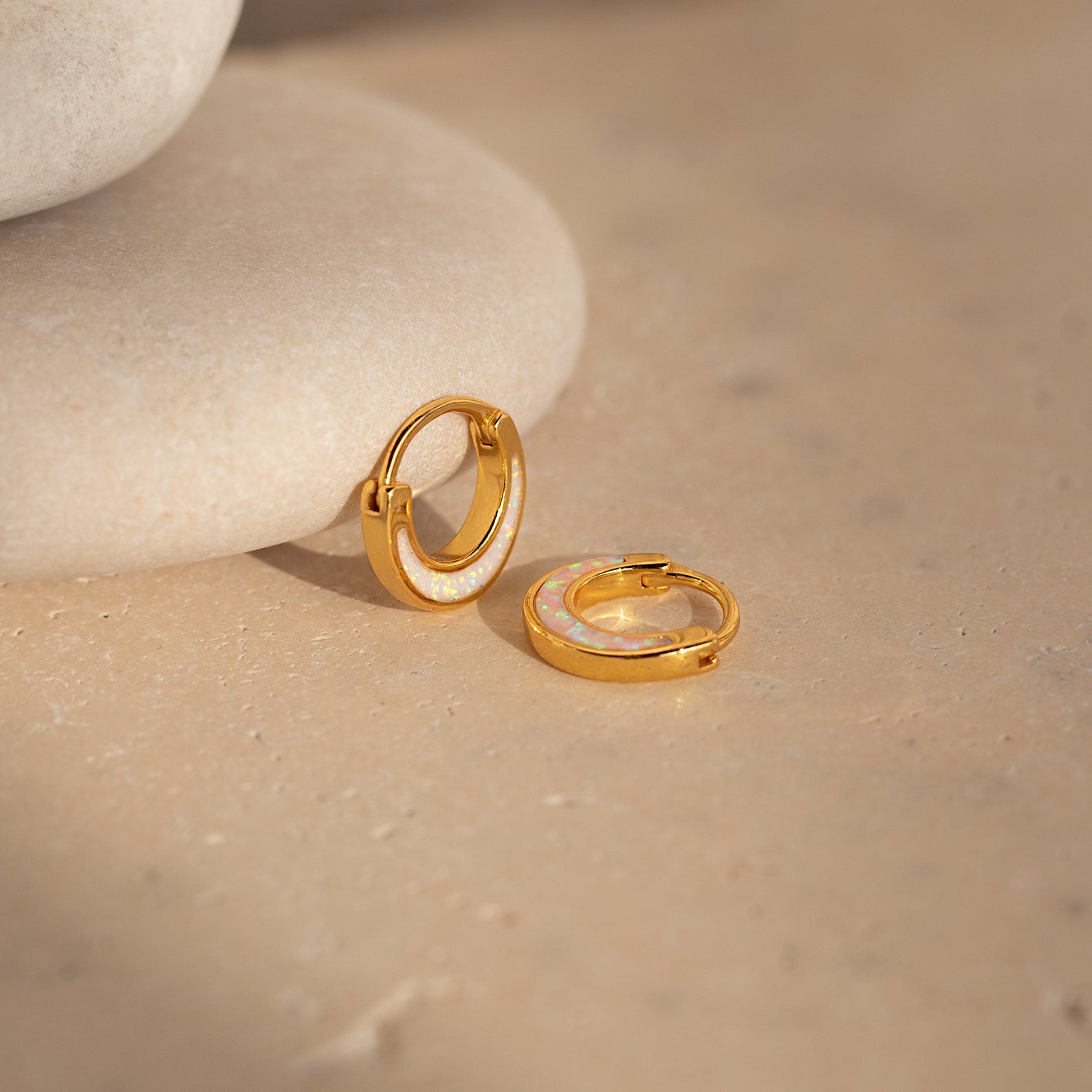 The Crescent Moon Opal Huggies glow elegantly atop a rock.
