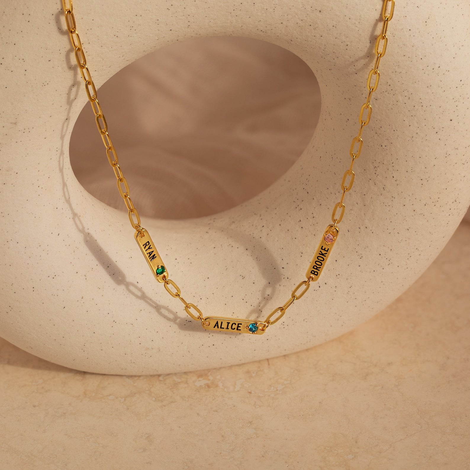 The Mini Name Birthstone Necklace features three engraved name tags—RIA, ALICE, BROOKE—each with a colored gem. This personalized bar necklace is a beautiful customized gift for your loved ones.