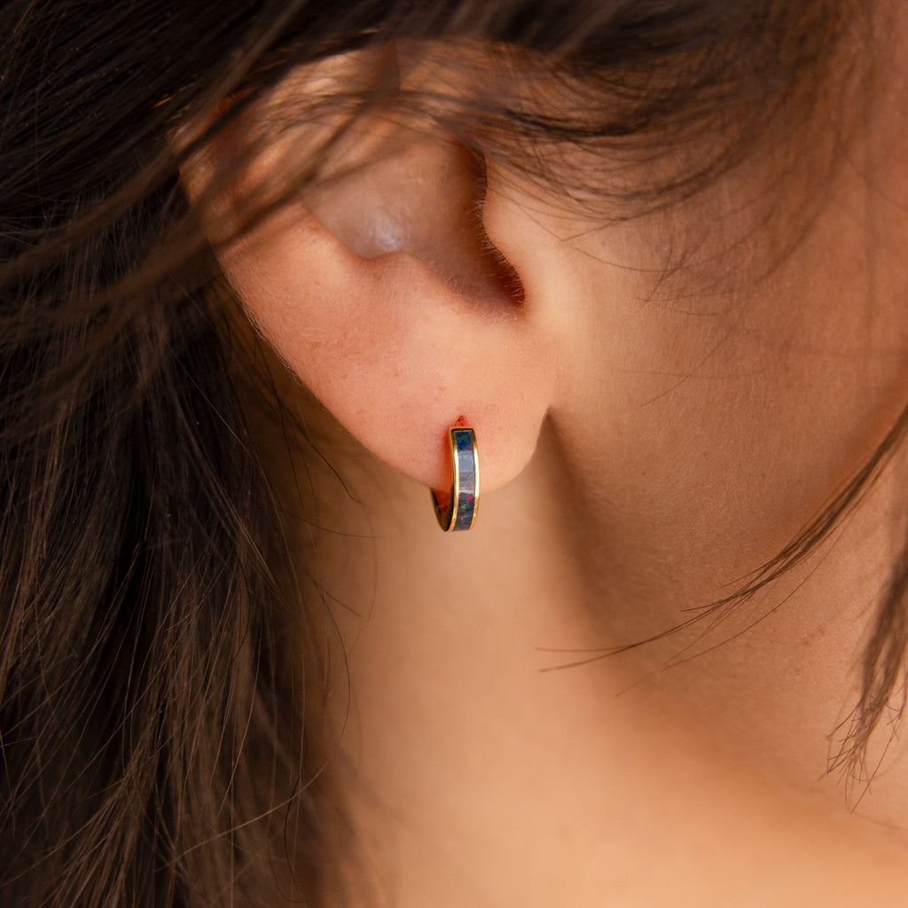 Close-up of a person’s ear adorned with a small, multicolored Opal Inlay Earring from the Opal Collection.
