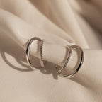 The Lydia Duo Cuffs—two silver hoop earrings with textured details—are elegantly displayed on soft beige fabric, perfect for pairing with multilayered earrings.