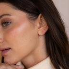 Woman with brown hair and natural makeup wears Tiny Zodiac Studs in gold Scorpio design, gazing to the side—ideal for creating a chic, personalized earring stack.