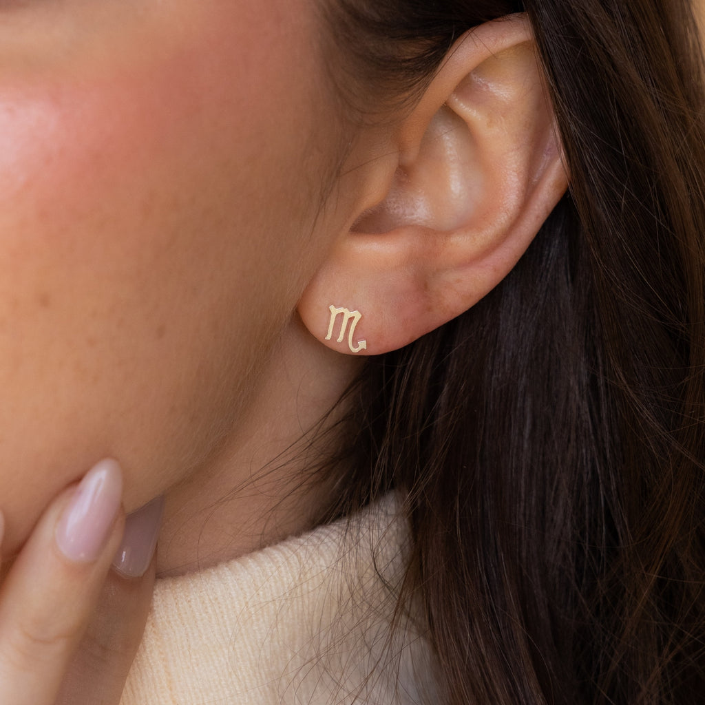 Close-up of a woman wearing Tiny Zodiac Studs in gold (Scorpio), gently touching her chin—a chic, personal touch for your earring stack or perfect for lovers of zodiac jewelry.