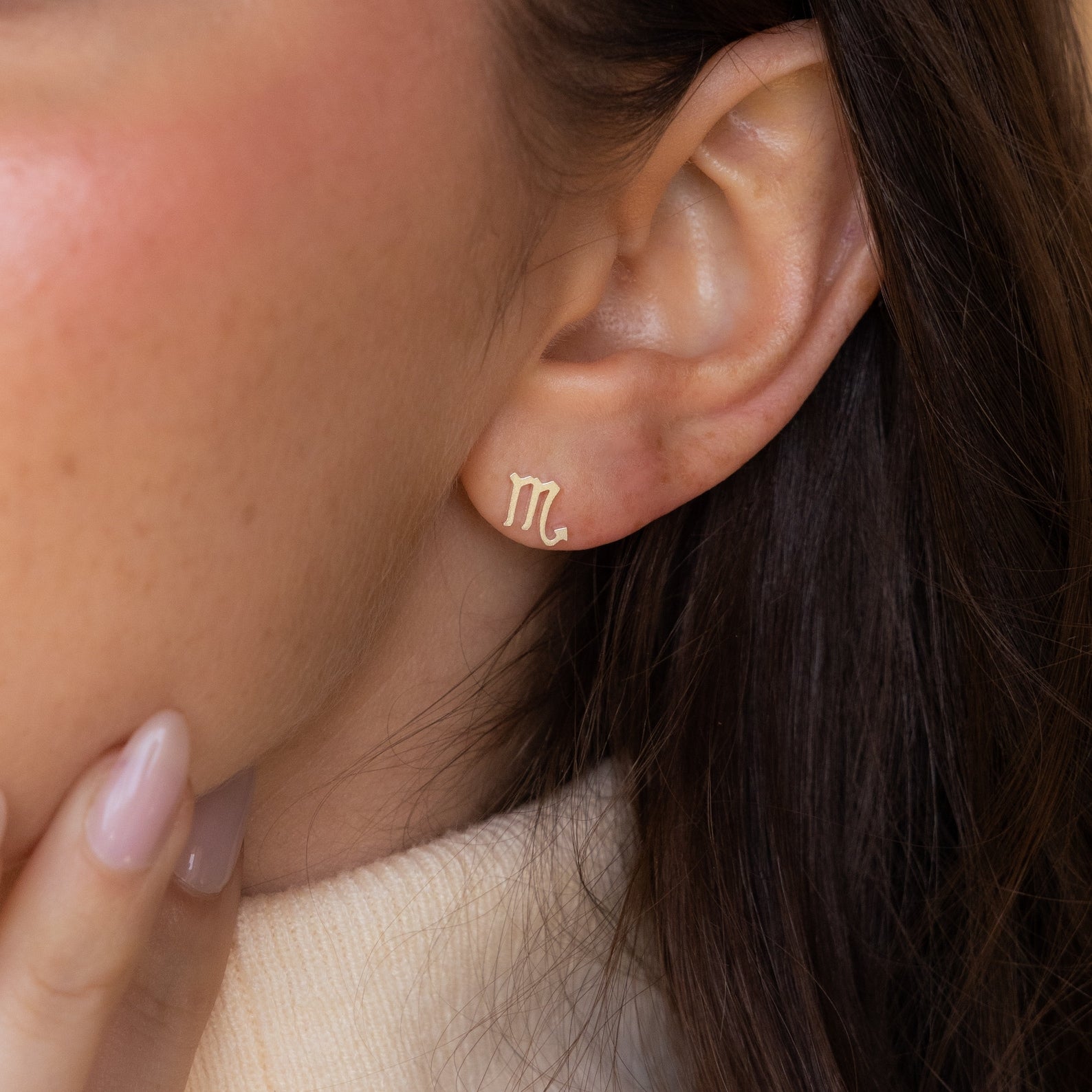 Close-up of a woman wearing Tiny Zodiac Studs in gold (Scorpio), gently touching her chin—a chic, personal touch for your earring stack or perfect for lovers of zodiac jewelry.