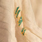 A pair of Opal Inlay Earrings with gold and turquoise details displayed on a soft, cream-colored fabric background.