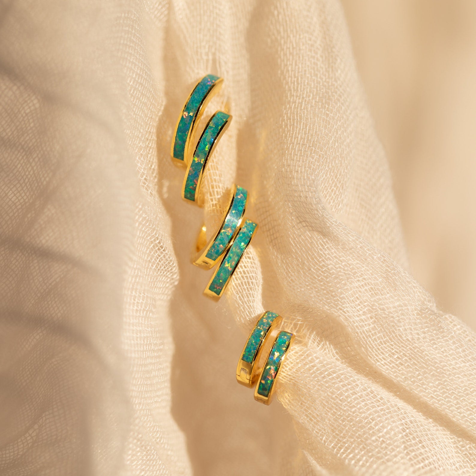 A pair of Opal Inlay Earrings with gold and turquoise details displayed on a soft, cream-colored fabric background.