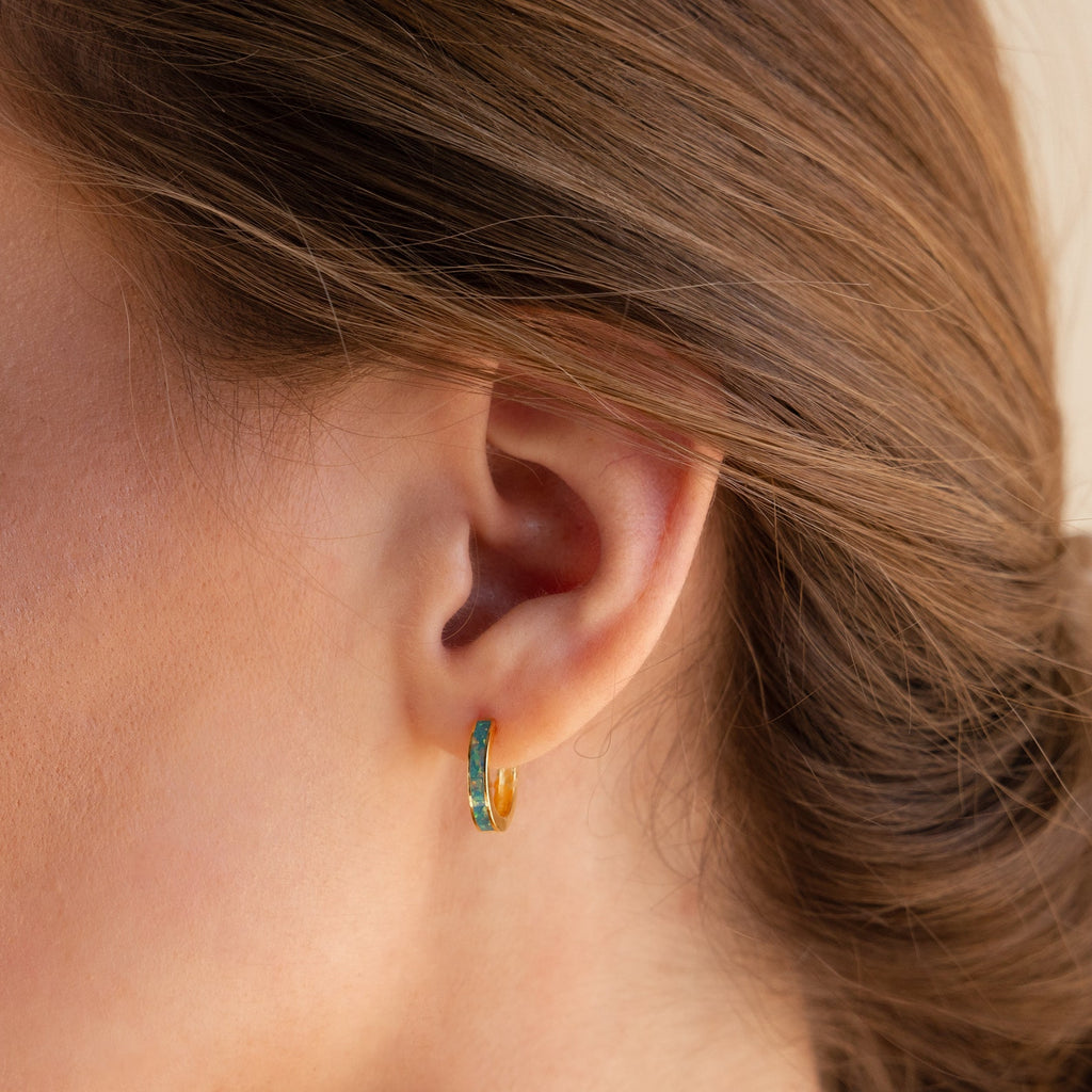 Close-up of a woman's ear wearing Opal Inlay Earrings—small gold and turquoise hoops from our Opal Collection—with brown hair pulled back.