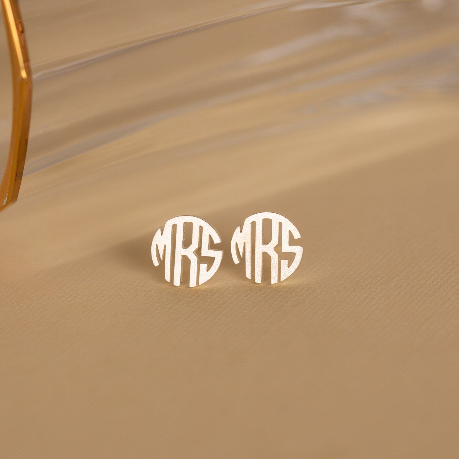Block Monogram Earrings in a silver round stud design engraved with "MRS," perfect for your earring stack, shown on a neutral beige background.