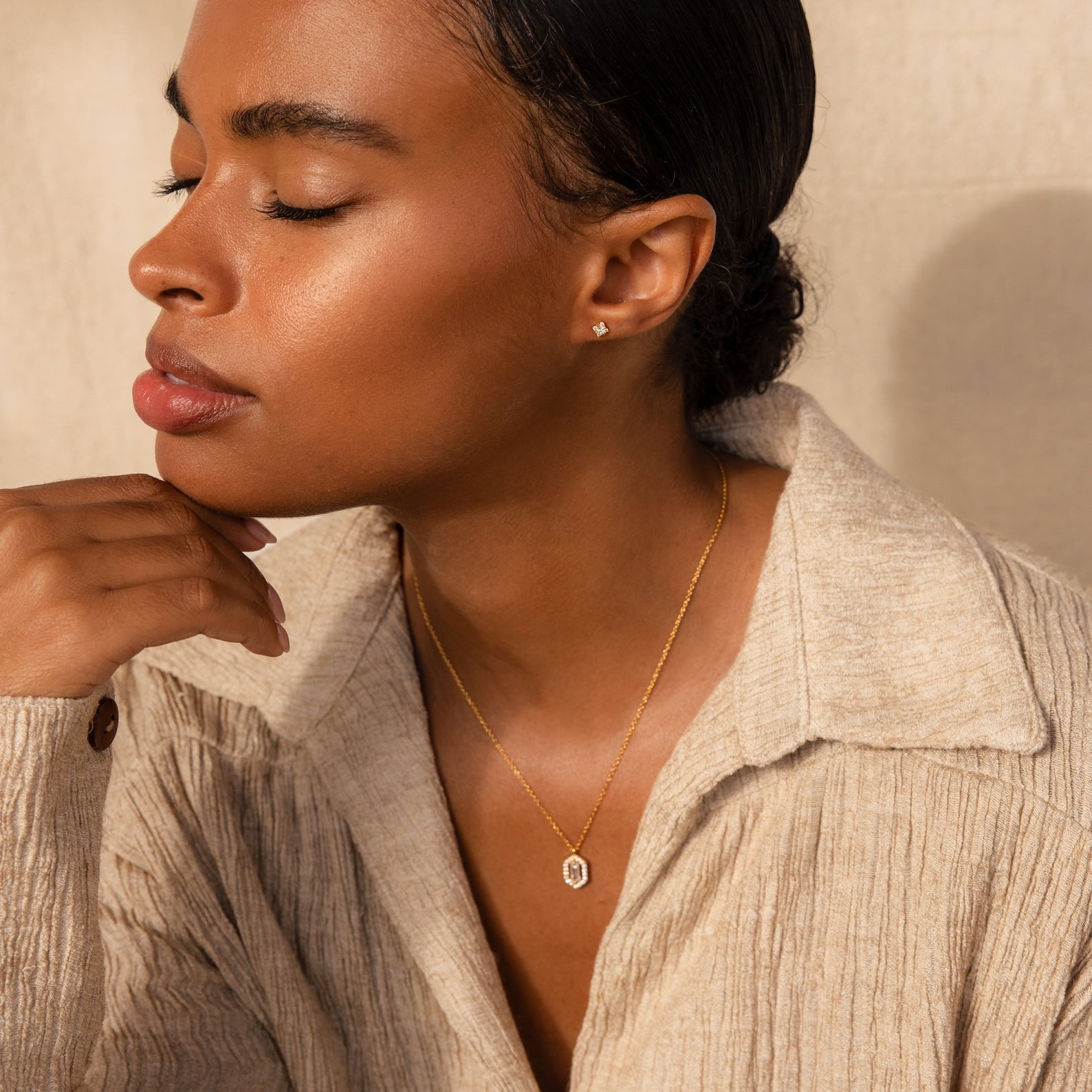 Woman with closed eyes wears a beige shirt and gold Daydreamer Diamond Studs earrings against a neutral background.