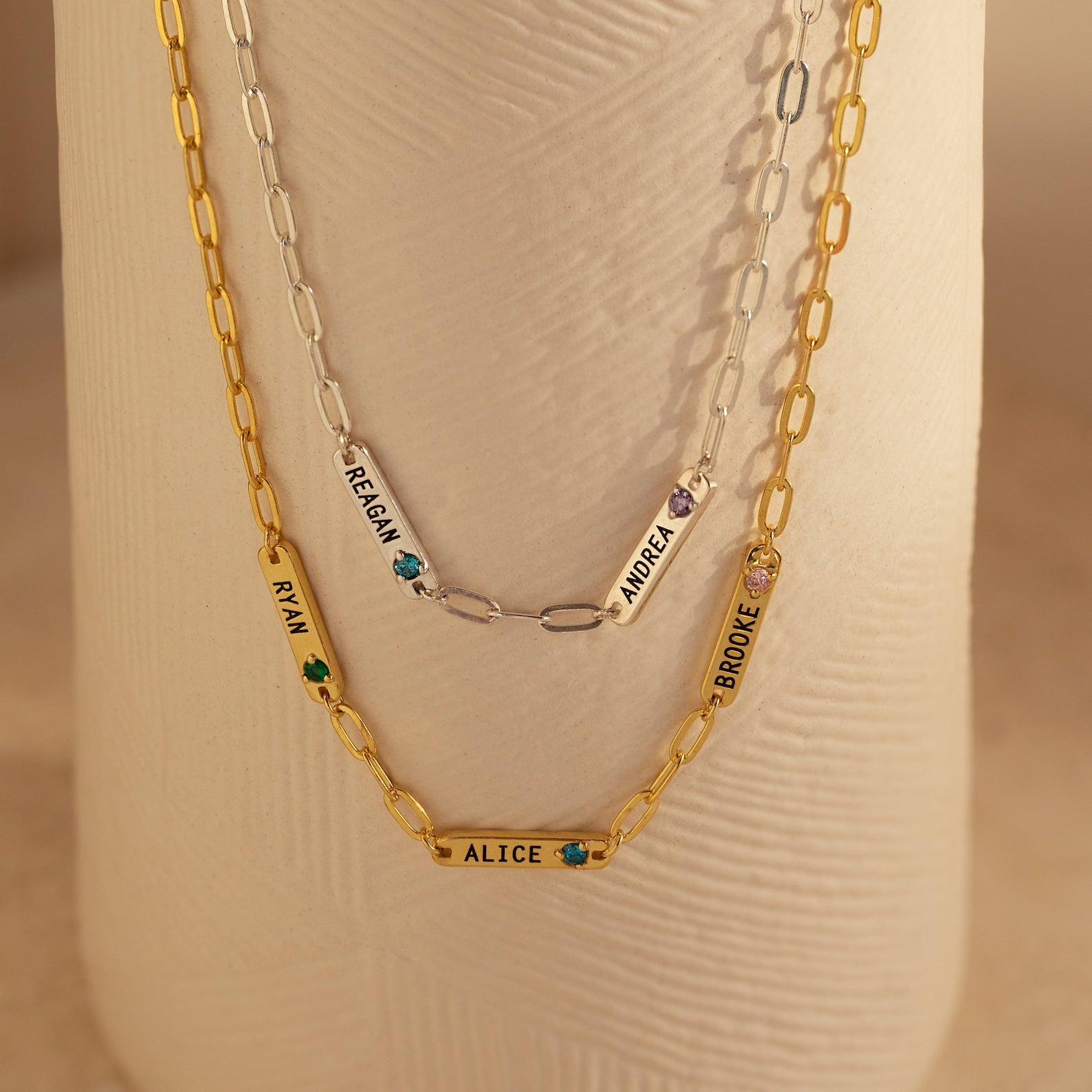 Two gold and one silver Mini Name Birthstone Necklaces featuring charms with names—RYAN, ALICE, REAGAN, ANDREA, BROOKE—are a perfect custom gift. Each paperclip chain adds a modern touch to this personalized accessory set.