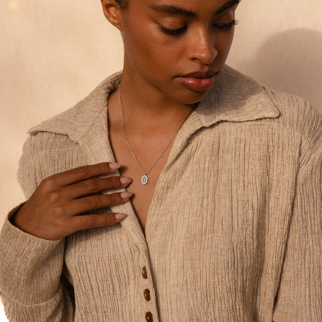 A woman wearing a textured beige shirt and the Daydreamer Diamond Necklace looks down with one hand on her chest, radiating timeless elegance.