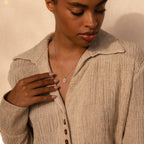 A woman wearing a textured beige shirt and the Daydreamer Diamond Necklace looks down with one hand on her chest, radiating timeless elegance.