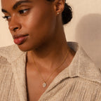 Woman exudes timeless elegance in a beige textured shirt, wearing the Daydreamer Diamond Necklace and stud earrings, gazing thoughtfully to the side.