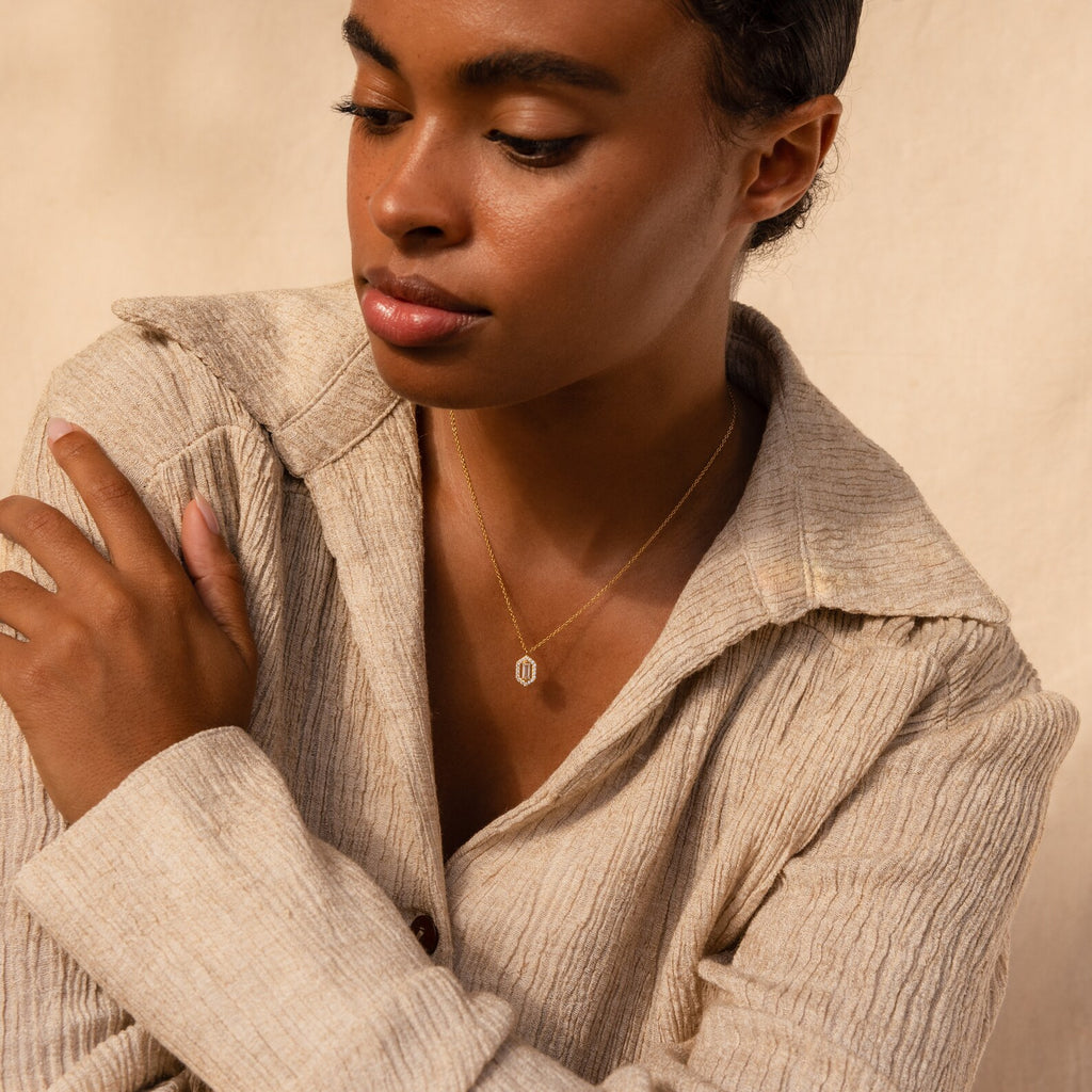 A woman in a beige textured shirt wears the Daydreamer Diamond Necklace, looking down with one arm across her body and radiating timeless elegance.