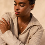 A woman in a beige textured shirt wears the Daydreamer Diamond Necklace, looking down with one arm across her body and radiating timeless elegance.