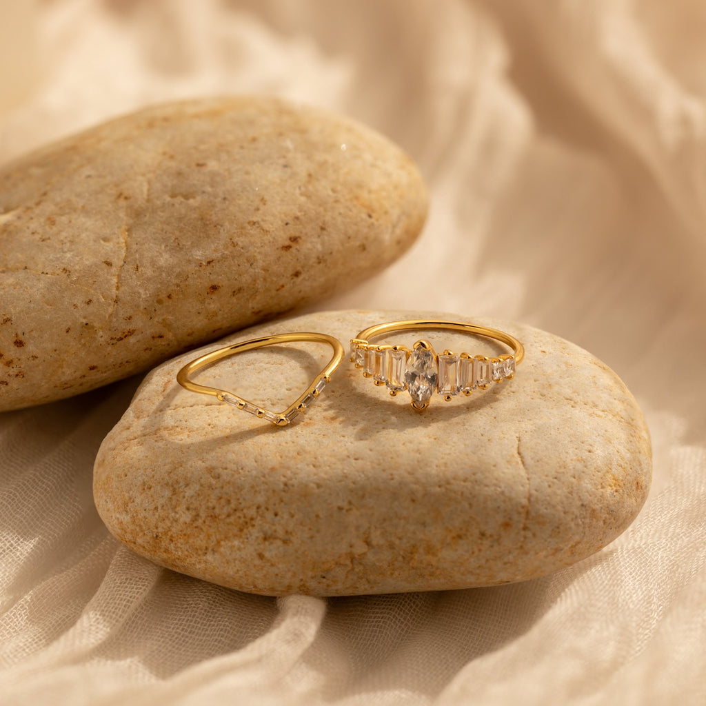 The Art Deco Ring Set features two gold rings displayed on smooth beige stones with a soft, light fabric background—perfect for showcasing timeless elegance.