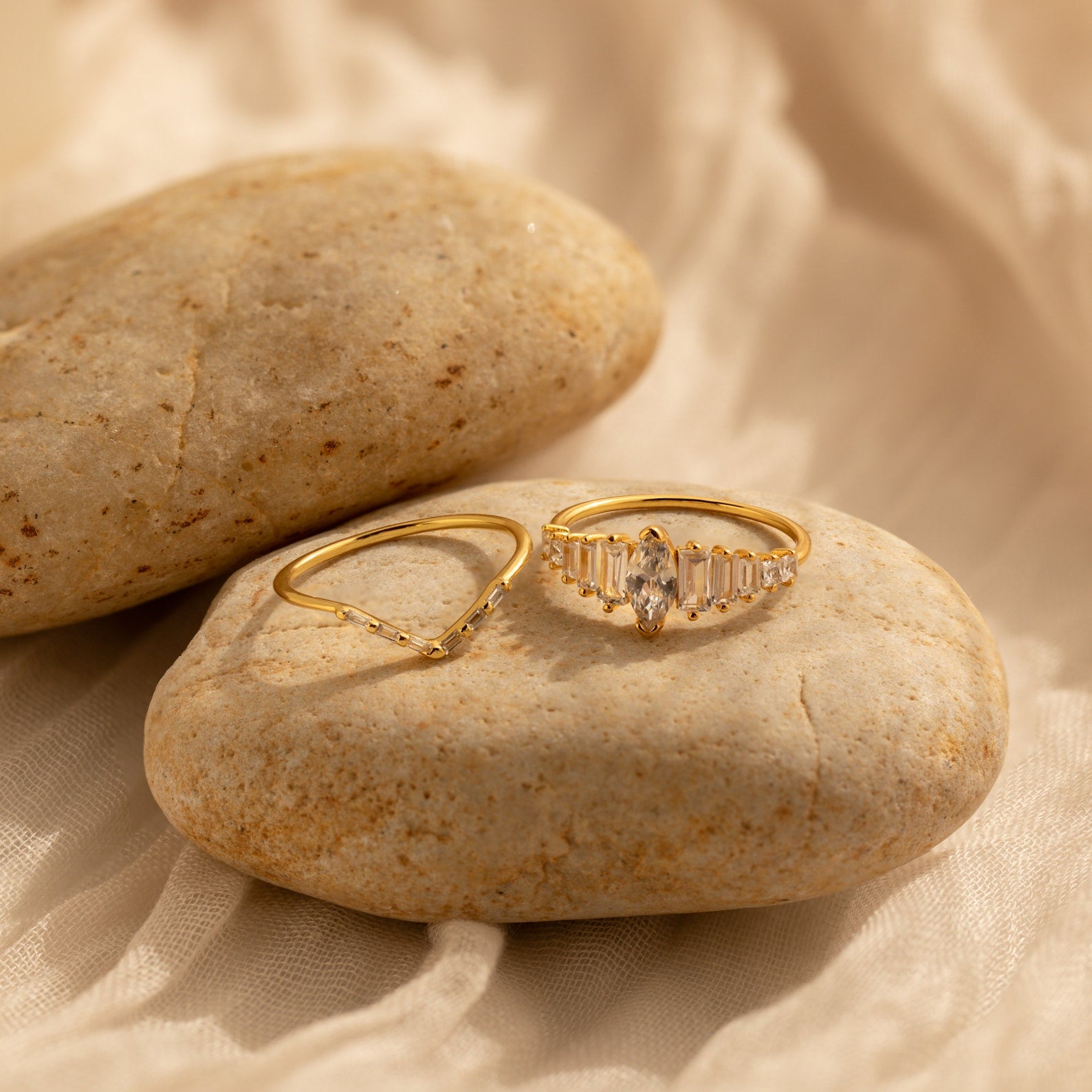 The Art Deco Ring Set features two gold rings displayed on smooth beige stones with a soft, light fabric background—perfect for showcasing timeless elegance.