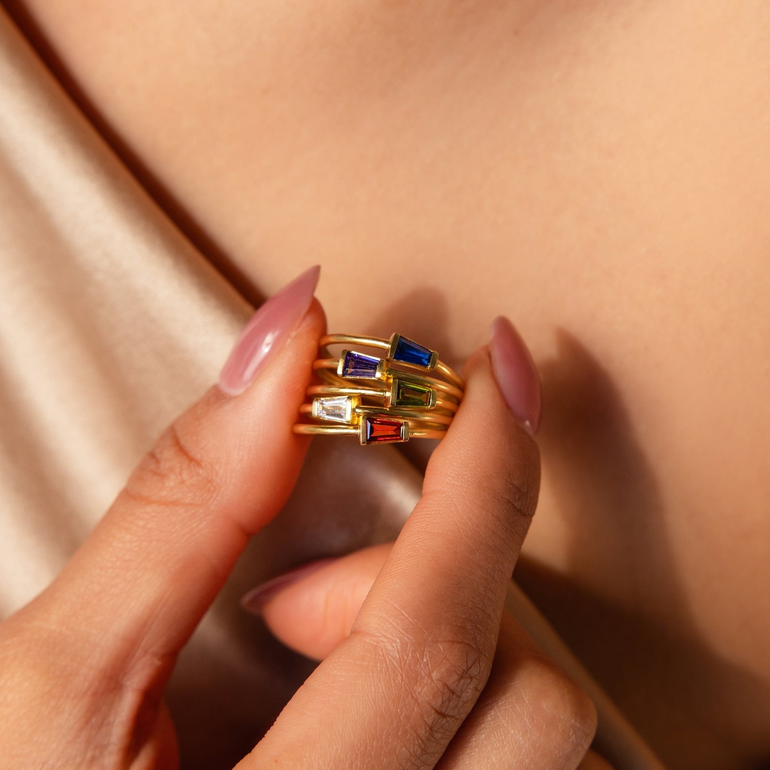 A manicured hand holds the Irregular Baguette Birthstone Ring, featuring colorful gemstone baguettes and an eye-catching irregular design against bare skin.