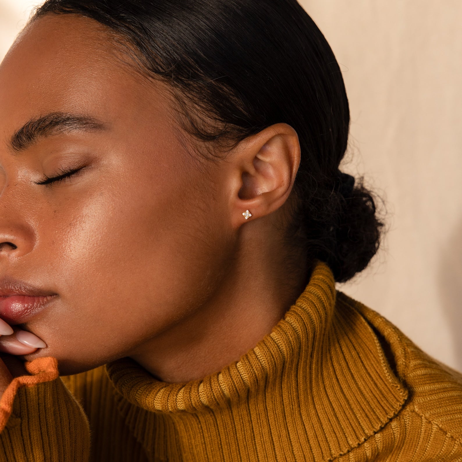 A woman in a mustard turtleneck with closed eyes showcases the Daydreamer Diamond Studs.