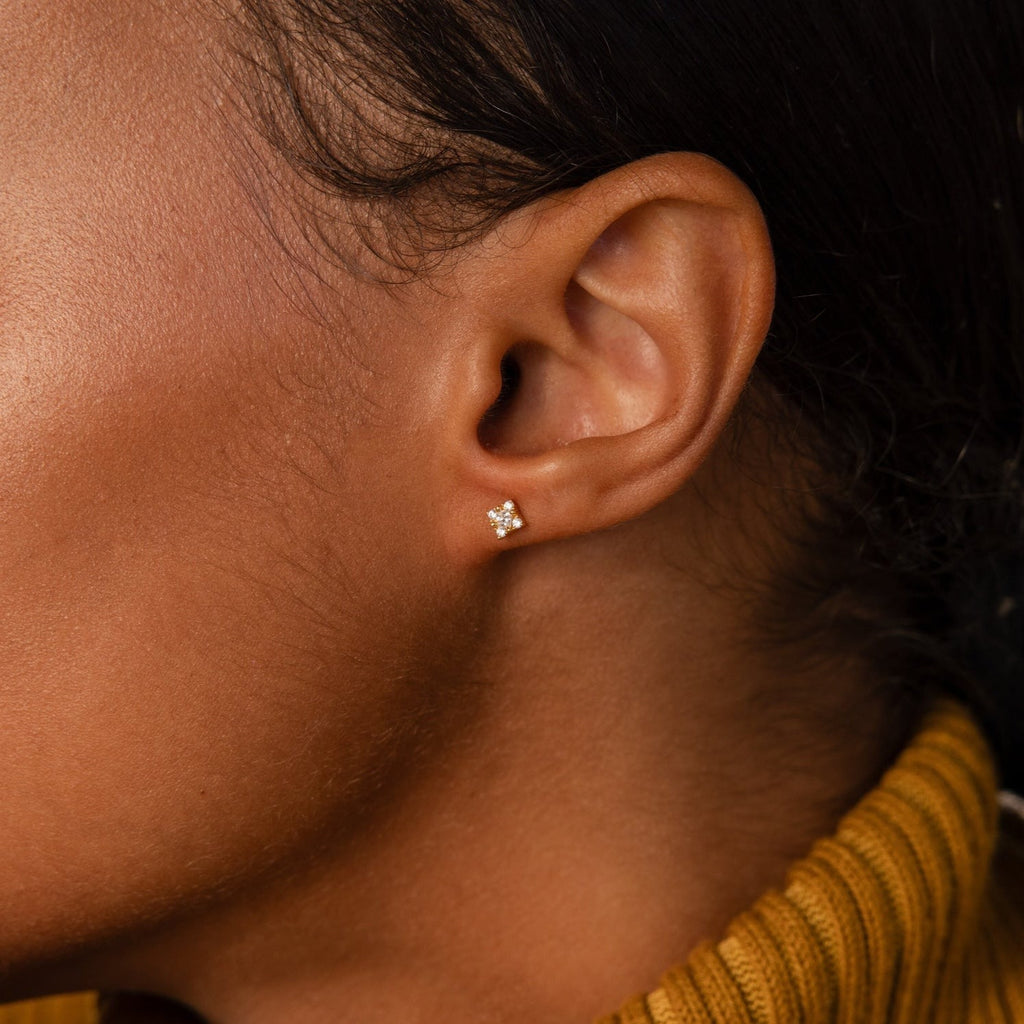Model wears gold Daydreamer Diamond Studs. The square-shaped earring features a shimmering diamond center with four more pave diamonds on each corner. 