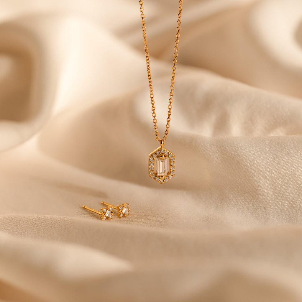 The Daydreamer Diamond Necklace features a hexagon pendant and matching stud earrings, displayed on soft beige fabric for a timelessly elegant and luxurious jewelry set.