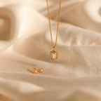 The Daydreamer Diamond Necklace features a hexagon pendant and matching stud earrings, displayed on soft beige fabric for a timelessly elegant and luxurious jewelry set.