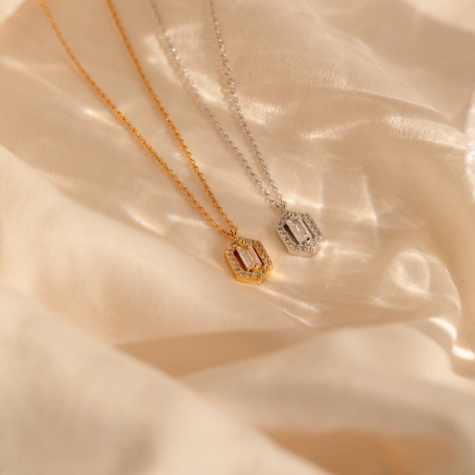 The Daydreamer Diamond Necklace, shown in both gold and silver with rectangular pendants on soft beige fabric, radiates timeless elegance and luxurious charm.