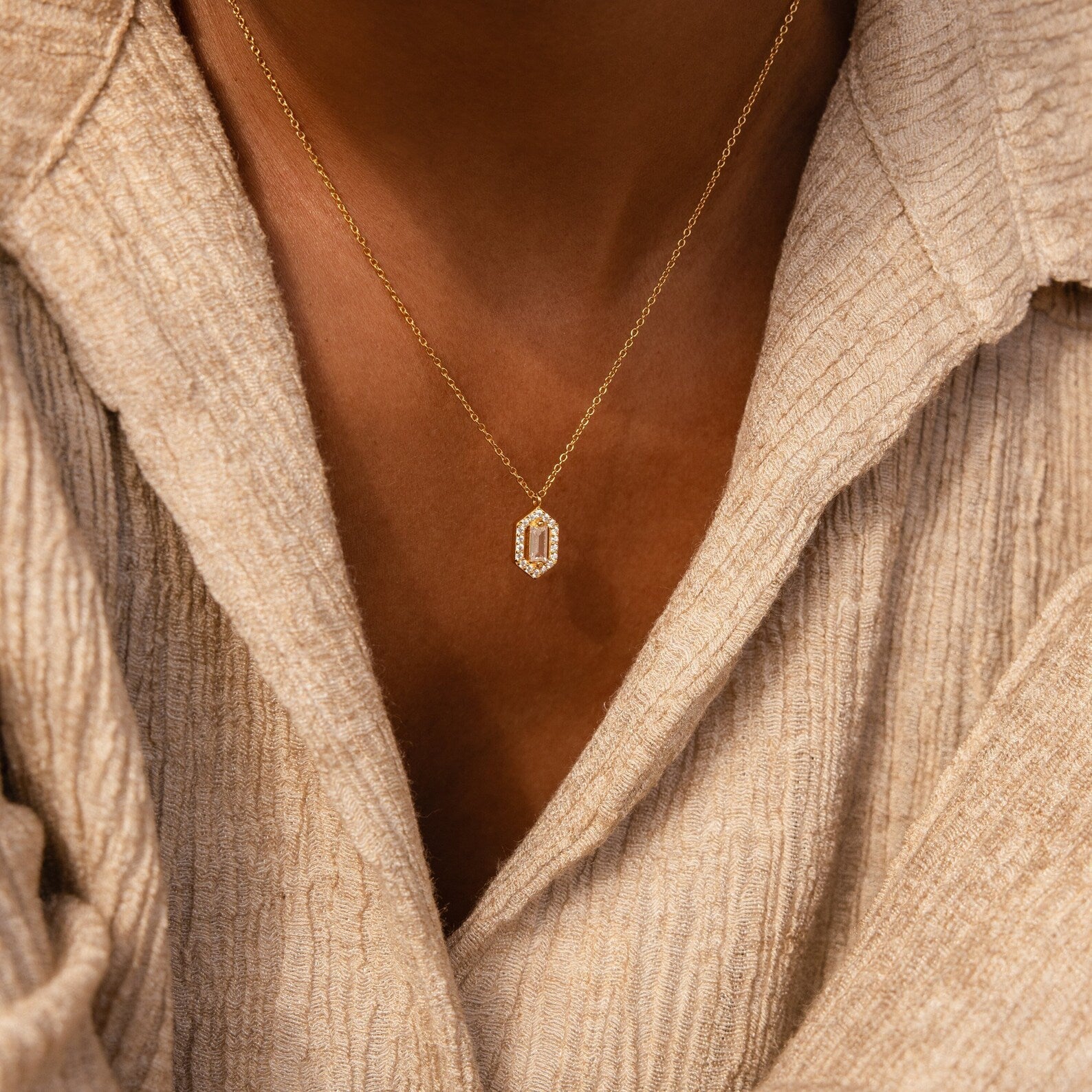The Daydreamer Diamond Necklace, featuring a small hexagonal pendant inspired by Art Deco style, adds elegance when layered over a beige textured shirt.