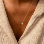 A close-up of the Art Deco Pendant Necklace, showcasing its gold chain and small kite pendant, worn over a beige textured top.