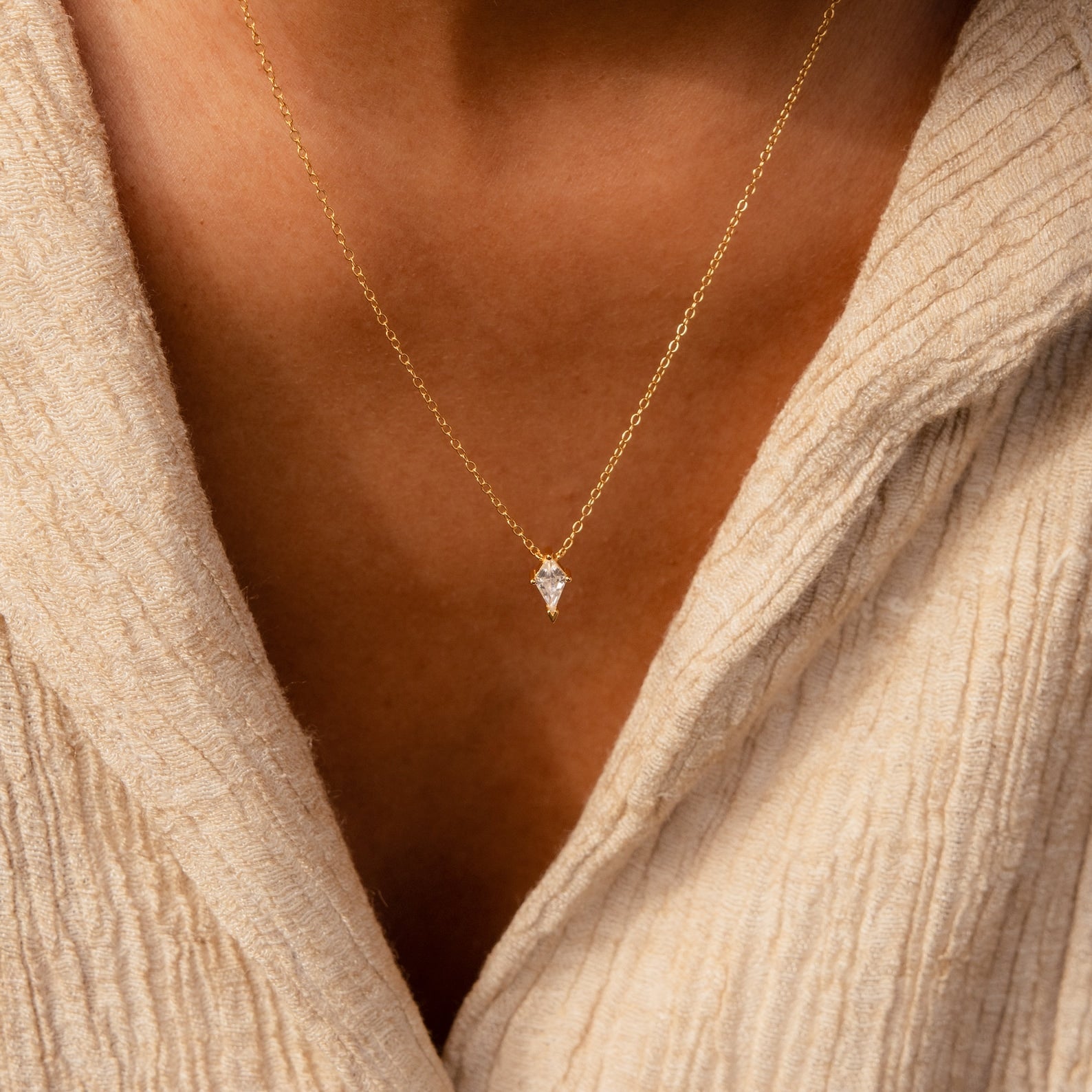 A close-up of the Art Deco Pendant Necklace, showcasing its gold chain and small kite pendant, worn over a beige textured top.