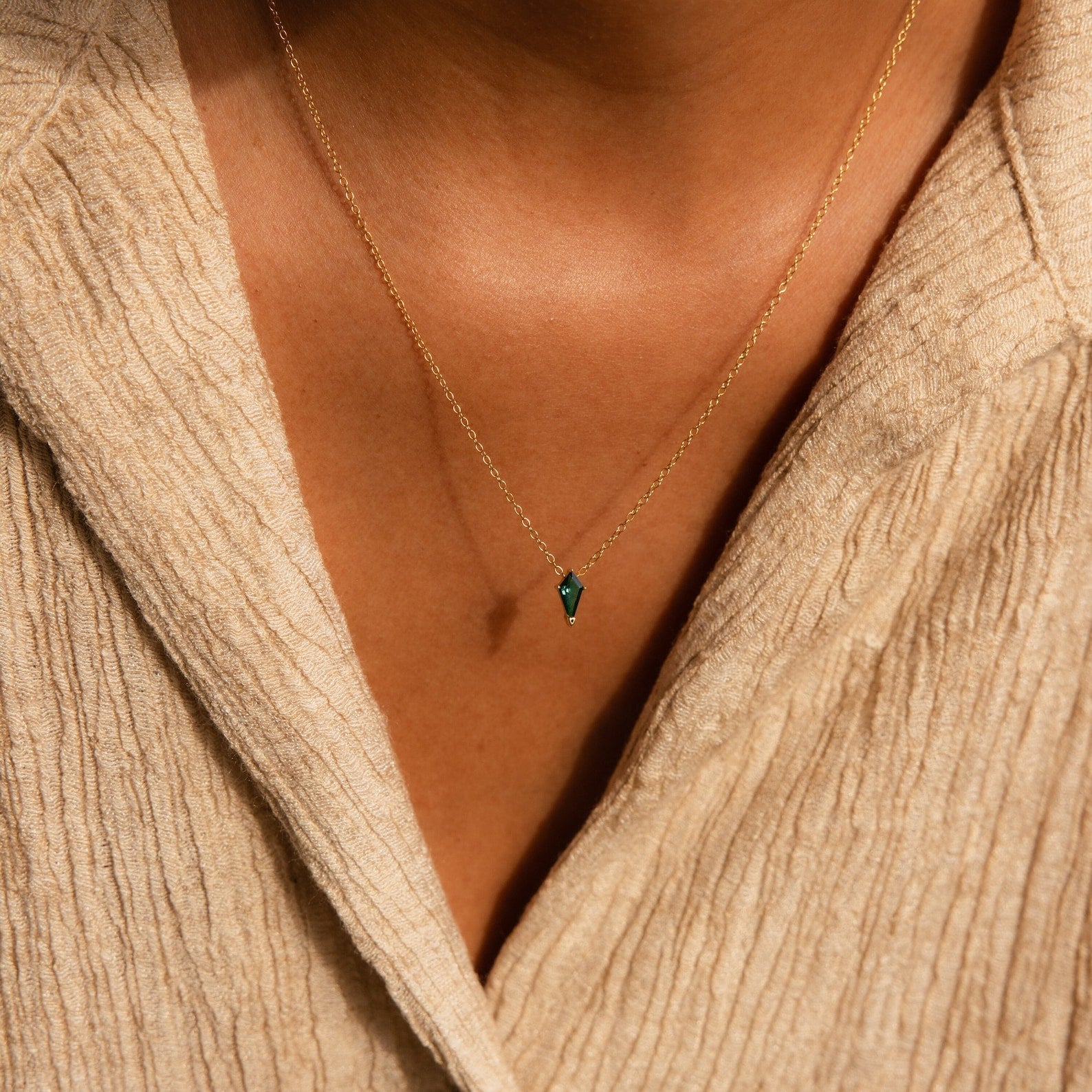 A person wearing the Art Deco Pendant Necklace featuring a small green pendant, paired with a beige textured shirt.