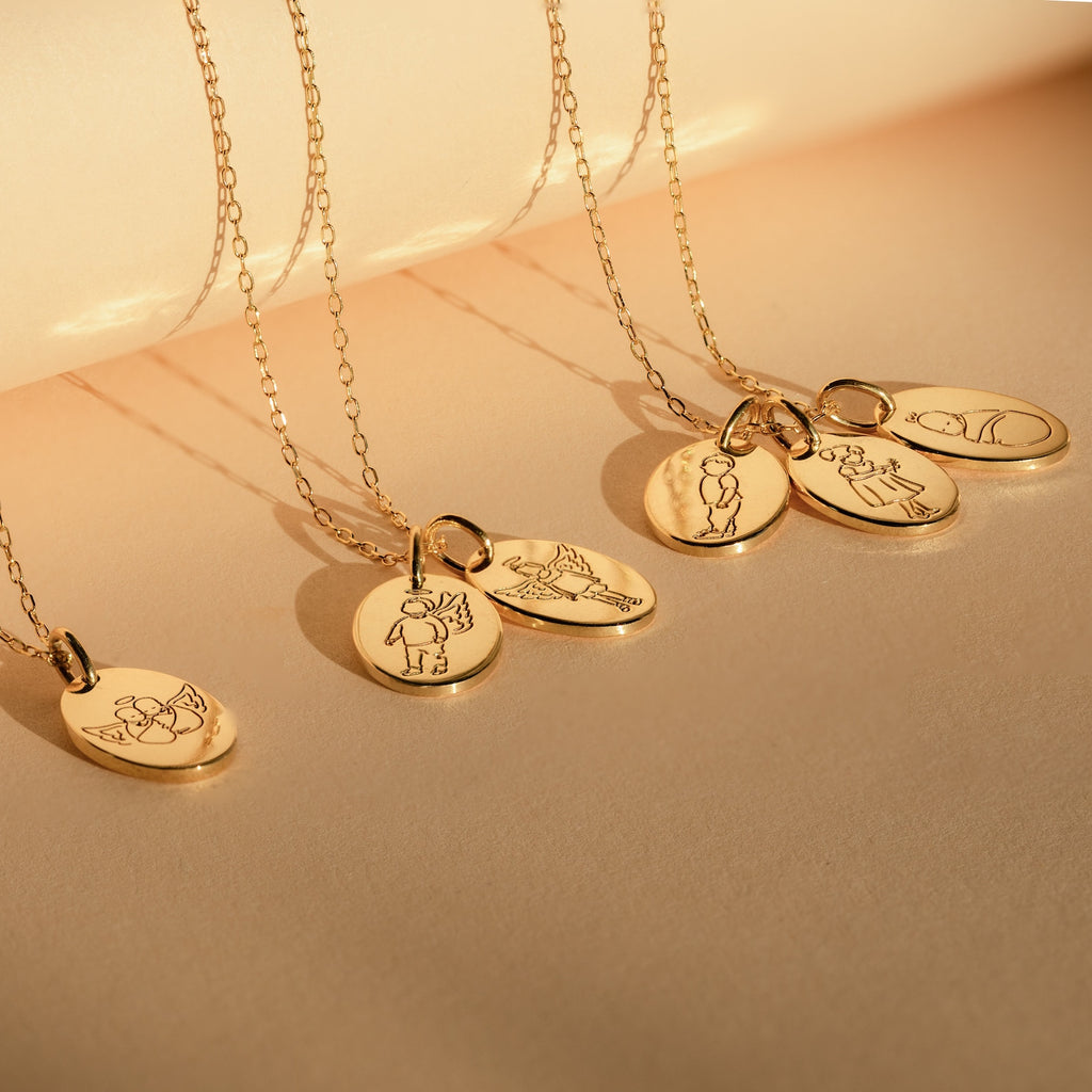 The Child Portrait Necklace is a gold engraved necklace with an oval pendant featuring minimalist line art of people or animals, ideal as a memorial piece or personalized keepsake, shown on a beige background.