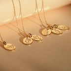 The Child Portrait Necklace is a gold engraved necklace with an oval pendant featuring minimalist line art of people or animals, ideal as a memorial piece or personalized keepsake, shown on a beige background.