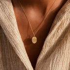 The Child Portrait Necklace, featuring an engraved pendant, is shown worn over a textured beige top on a person's neck and chest.
