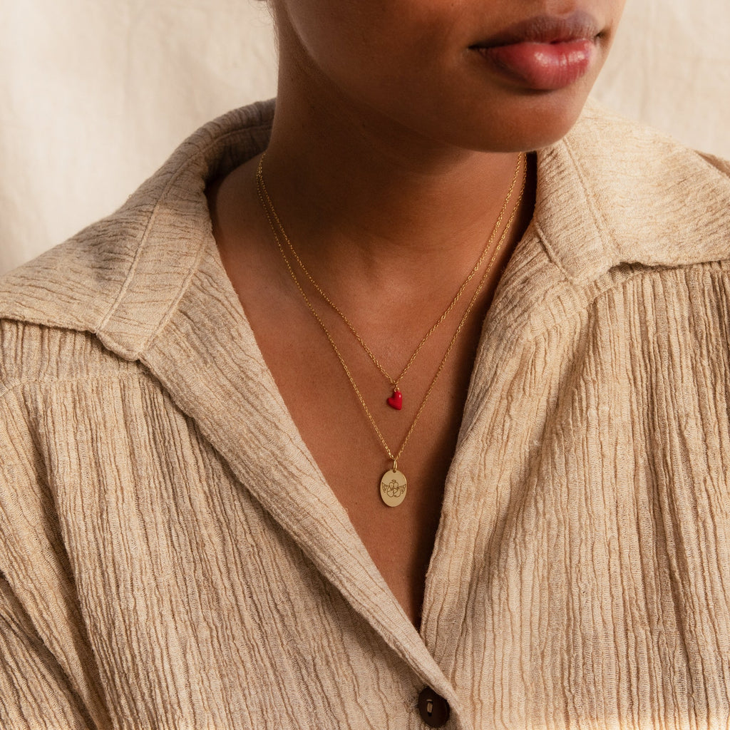 Woman wearing a beige textured shirt and two gold necklaces: one with a red stone and one featuring the Child Portrait Necklace, an engraved necklace with a round pendant.