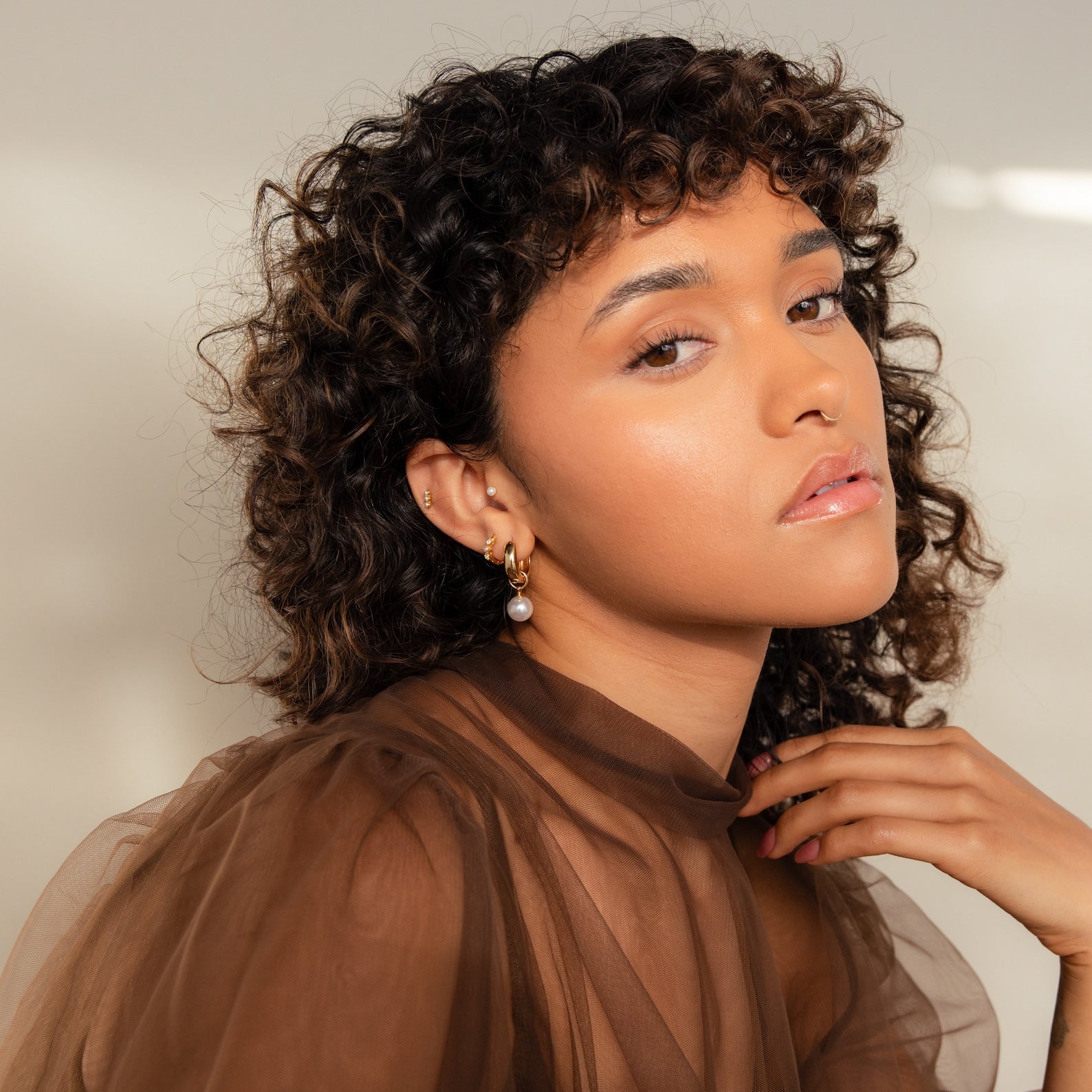 Woman with curly hair in a sheer brown top, wearing Bold Pearl Drop Earrings, looking at the camera.