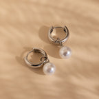 Bold Pearl Drop Earrings featuring silver hoops with dangling white pearls, perfect as statement pieces, showcased on a soft beige textured background.