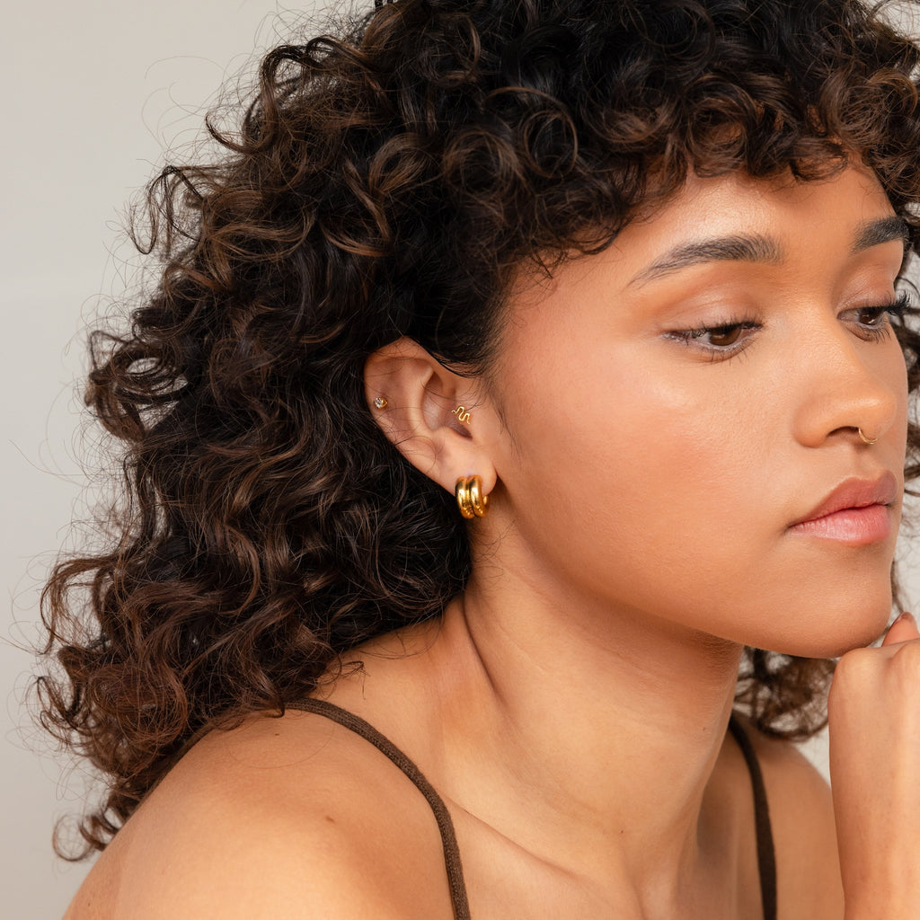 A woman with curly hair wears Chunky Double Hoops, highlighting these bold earrings as an elegant statement piece.