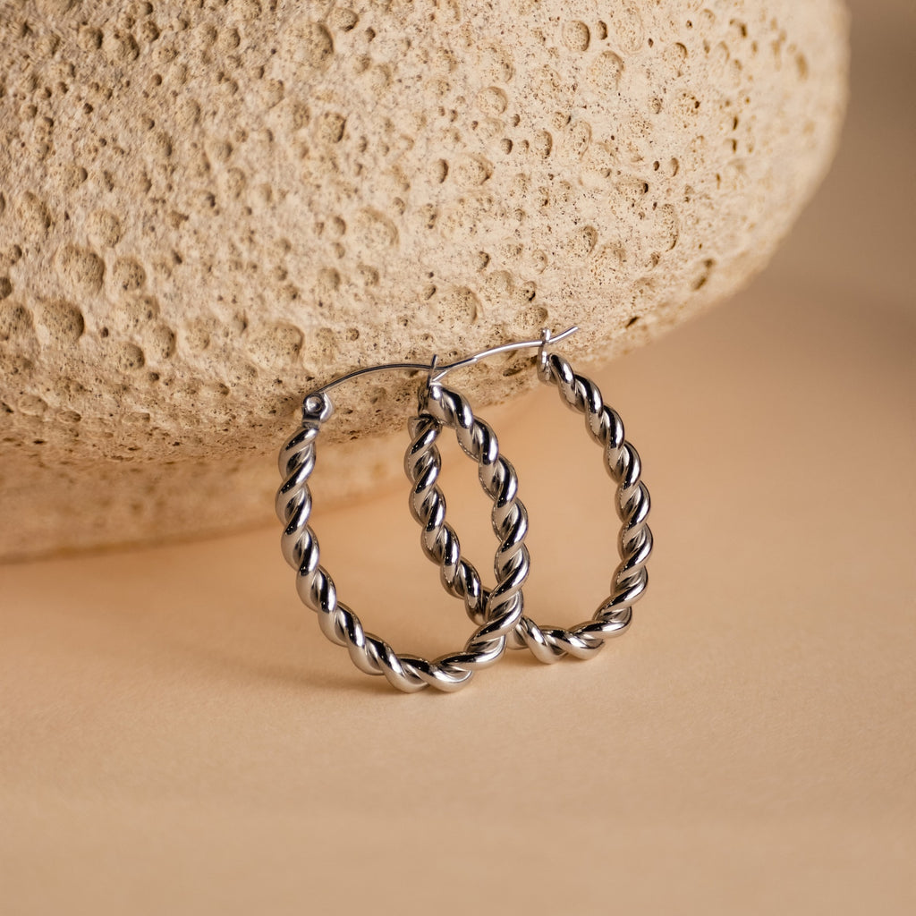 Bold Twisted Hoops displayed on a textured beige stone background, highlighting their elegant twist design and minimalist style.