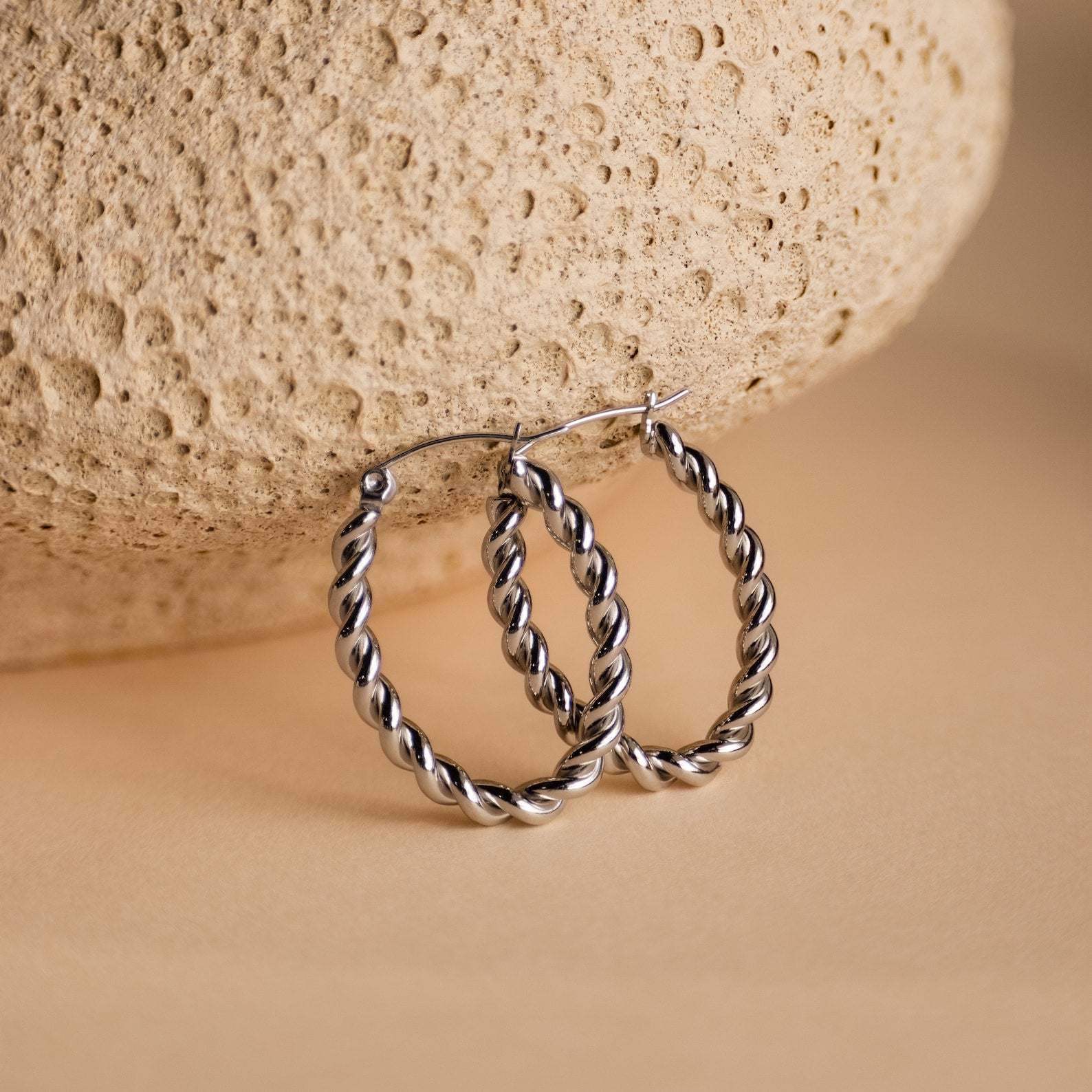 Bold Twisted Hoops displayed on a textured beige stone background, highlighting their elegant twist design and minimalist style.
