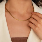A woman wearing a cream blazer and minimalistic jewelry—a Multi Strand Chain Necklace—gently touches the necklace with her right hand.