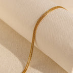 The Multi Strand Chain Necklace, a minimalistic jewelry piece, is elegantly showcased on a textured cream-colored fabric background.