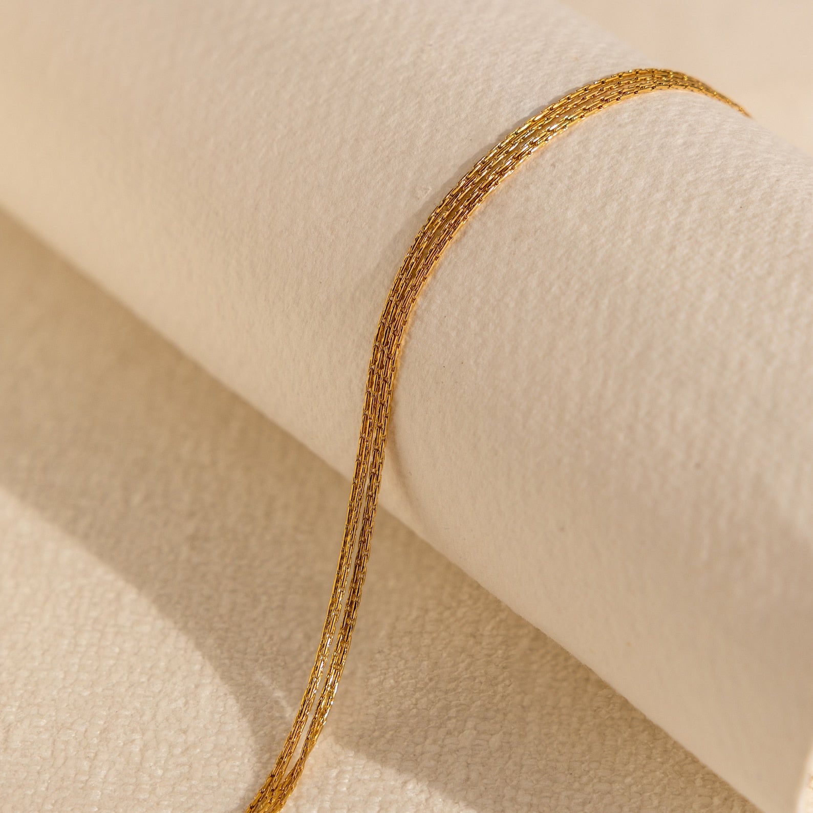 The Multi Strand Chain Necklace, a minimalistic jewelry piece, is elegantly showcased on a textured cream-colored fabric background.